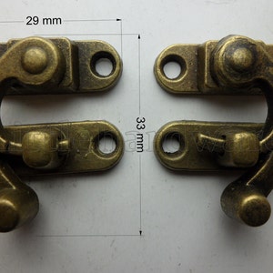 May include: Two antique brass-finished hook and eye clasps, each measuring 29 mm wide and 33 mm long. The clasps have a rounded, decorative design.
