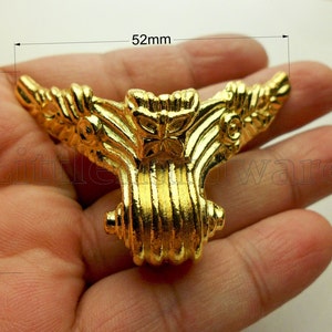 Op de afbeelding: Een gouden metalen hoekbeugel met een decoratief bloemmotief. De beugel meet 40 mm bij 52 mm.