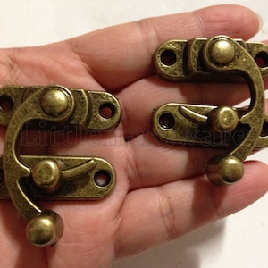 May include: Two antique brass-toned metal clasps with a hook and latch mechanism. The clasps have a distressed finish and are ideal for adding a vintage touch to craft projects.