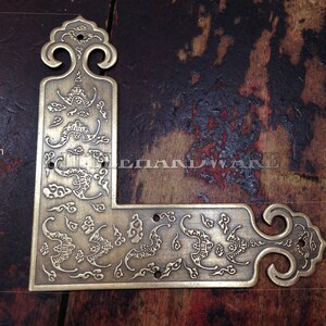 Puede incluir: Un soporte de esquina de latón en forma de L con diseños ornamentados de nubes y flores. El soporte mide 9 cm por 2,5 cm. El herraje tiene una estética vintage, adecuado para muebles o aplicaciones decorativas.