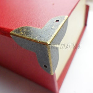 May include: A close-up of a corner of a red box with a black and gold metal corner protector. The corner protector has two visible screws.