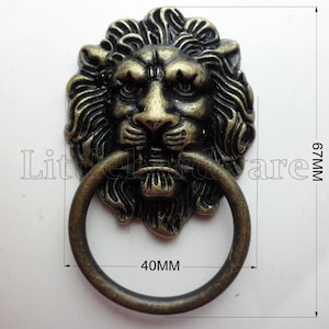 以下が含まれることがあります： リングハンドル付きのアンティークブロンズライオンヘッドドアノッカー。ライオンの頭は精巧に作られており、リングハンドルは直径40mmです。ノッカーの高さは6.7cmです。