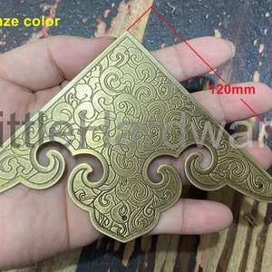 Könnte beinhalten: Eine bronzene Eckkonsole mit einem dekorativen floralen Design. Die Konsole ist 120 mm lang.