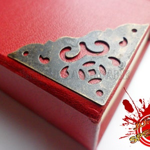 May include: A red leather-bound journal with a decorative metal corner piece. The corner piece is ornate and has a cut-out design.