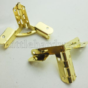 Può includere: Due cerniere d'angolo dorate, ciascuna con tre sezioni che si ripiegano insieme. Le cerniere sono progettate per collegare due pezzi di legno ad un angolo di 90 gradi.