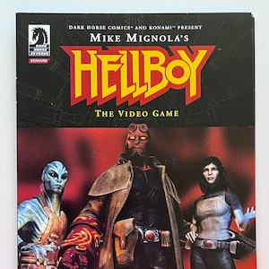 May include: A video game cover featuring Hellboy, a red-skinned demon with horns, a blue-skinned alien, and a woman with dark hair. The cover is black with yellow text that reads "Mike Mignola's Hellboy The Video Game" and "Coming in Fall 2007".