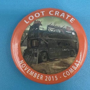May include: Round orange button with the text "LOOT CRATE" at the top and "NOVEMBER 2015 - COMBAT" at the bottom. The center image depicts a double-decker bus with a post-apocalyptic design.