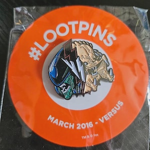 May include: A circular orange backing card with the text #LOOTPINS, MARCH 2016 - VERSUS, and TM & © Fox. Attached is a metal enamel pin featuring a split design of an Alien and a Predator head separated by a white lightning bolt symbol.