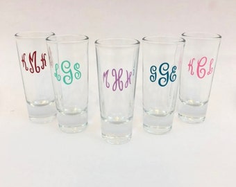 Może przedstawiać: Pięć przezroczystych szklanek do shotów z różnokolorowymi monogrammi. Monogramy to "HSM", "LGS", "MXH", "GGE" i "HCL".