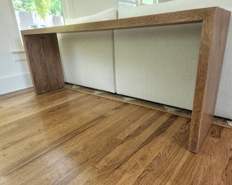 Könnte beinhalten: Ein langer, rechteckiger Holz-Konsolentisch mit einer natürlichen Holzoptik. Der Tisch steht vor einem weißen Sofa.