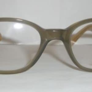May include: A pair of brown eyeglasses with clear lenses and the text "Gianni Versace" printed on the right lens.