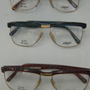Puede incluir: Tres pares de gafas con monturas doradas y lentes transparentes. Las monturas son de carey, verde y plástico burdeos. Las lentes están etiquetadas con "Elite" y "L'Amy".