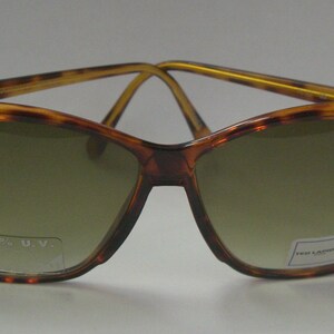 May include: Tortoise shell sunglasses with gold accents and brown lenses. The sunglasses have the text "100% U.V." printed on the right lens and "Fred Laudon" printed on the left lens.