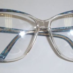 Puede incluir: Gafas de plástico transparente con montura azul y dorada. La montura tiene forma de ojo de gato y las lentes son transparentes.