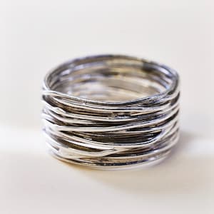 May include: A wide band ring constructed from multiple thin, interconnected silver-toned wires. The design features a layered, overlapping structure with a polished finish and darkened recessed areas between the individual wire strands.