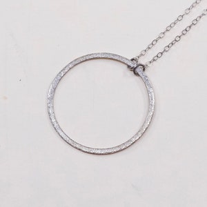 May include: A silver-toned necklace featuring a textured, open circle pendant. The pendant is connected to a delicate chain. The design is simple and elegant, suitable for everyday wear or special occasions.