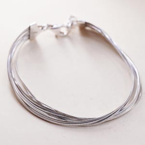 May include: A silver bracelet with multiple strands, featuring a textured, woven design. The bracelet has a secure clasp and is displayed against a neutral background. This piece of jewelry is suitable for everyday wear.