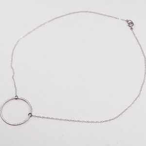 May include: A delicate silver necklace featuring a circular pendant. The pendant is connected to a fine chain that fastens with a small clasp. The necklace is displayed on a white background, highlighting its minimalist design.