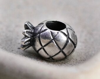 May include: A silver-colored charm in the shape of a pineapple. The charm has a textured surface with a diamond pattern and a small opening at the top. The pineapple's crown is detailed with several leaves.