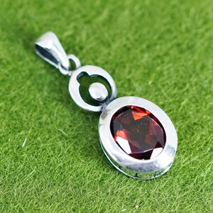 May include: A silver pendant with a large, oval-cut, deep red gemstone. The pendant has a simple, elegant design with a loop at the top for a chain. The gemstone is set in a silver bezel.
