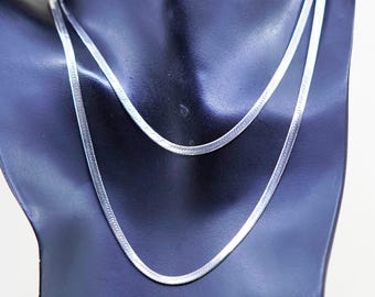 Puede incluir: Dos collares de plata con diseño de espiga, exhibidos en un maniquí negro. Los collares son de diferentes longitudes y presentan un diseño plano y tejido. Las cadenas son brillantes y reflejan la luz, creando una apariencia elegante. Joyería clásica.