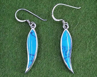 May include: A pair of silver earrings with a teardrop shape. Each earring features a vibrant turquoise stone with dark blue veining, set in a polished silver frame. The earrings have a simple hook design for pierced ears.