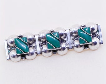 Puede incluir: Pulsera plateada con tres incrustaciones rectangulares de piedra de color turquesa con un diseño de cuerda trenzada. La pulsera tiene una serie de esferas plateadas y eslabones rectangulares. La joya se muestra sobre un fondo claro.