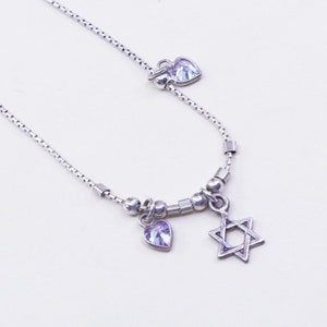 May include: A silver necklace featuring a Star of David pendant and a heart-shaped charm with a light purple gemstone. The necklace has a delicate chain design with small beads and square links.
