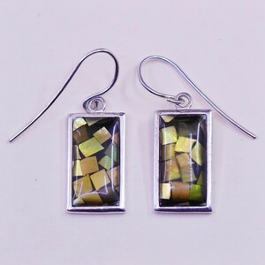May include: A pair of rectangular dangle earrings. Each earring features a mosaic of iridescent, square-cut pieces in shades of gold, green, and brown, set within a silver-colored frame. The earrings have a simple hook design.