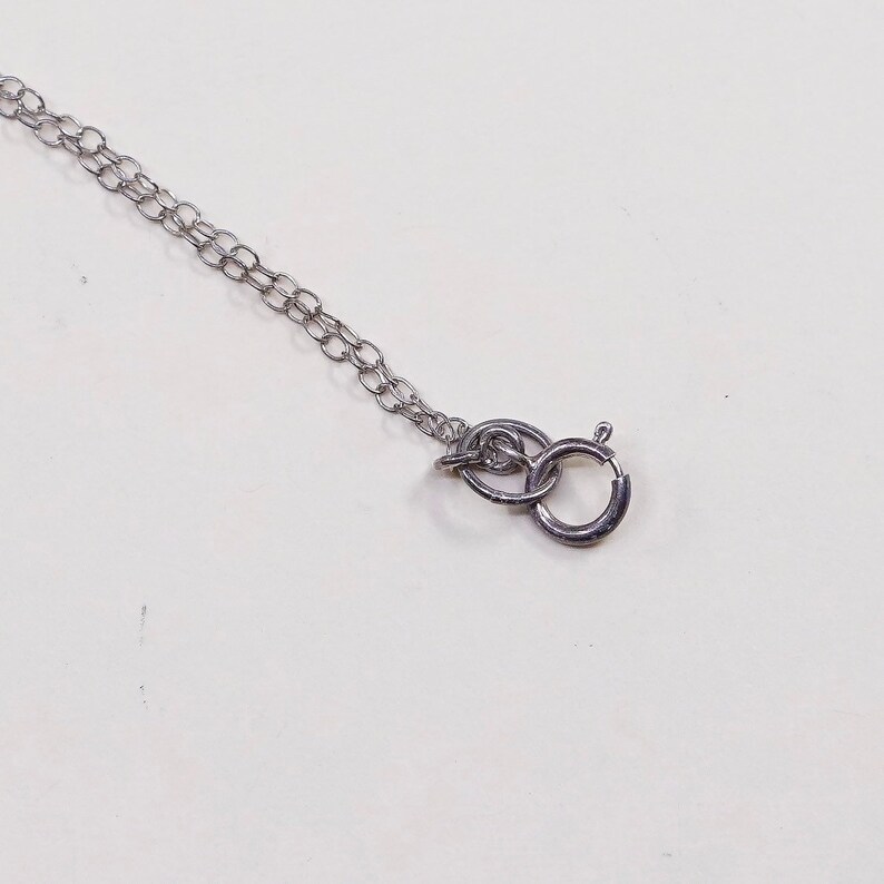 May include: A silver-colored necklace chain with a lobster clasp. The chain is made of small, interconnected oval links. The clasp is a simple, secure design, perfect for attaching to a pendant or charm. The necklace is shown against a white background.