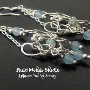 Peut inclure: Une paire de longues boucles d'oreilles pendantes en argent avec des perles de verre bleu clair et des accents de fil. Les boucles d'oreilles sont réalisées par Fluid Metals Studio, Uniquely You Art Jewelry.