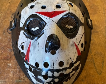 May include: A white hockey mask with black and red paint details. The mask has a skull design with eye holes and a black strap.