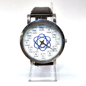 May include: A silver and black wristwatch with a white face. The face features a stylised atom with a blue nucleus and orbiting electrons. The face also features a circle of chemical element squares, including hydrogen, helium, lithium, beryllium, boron, carbon, nitrogen, oxygen, fluorine, neon, sodium, and magnesium.