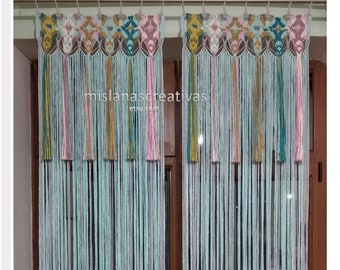May include: Two macrame curtains with a geometric pattern in shades of pink, teal, and yellow. The curtains are hanging in a window and have long, flowing strands.