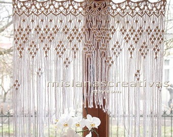 May include: White macrame curtain with a geometric pattern hangs in a window. A white orchid plant sits on the windowsill.