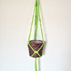 May include: A lime green macrame plant hanger with a brown woven pot hanging from it. The hanger has long tassels at the bottom.