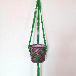 May include: A green macrame plant hanger with a brown woven pot hanging from it.