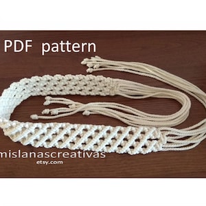 Könnte beinhalten: Cremefarbener Makramee-Gürtel mit geometrischem Design und langen, geknoteten Quasten. Der Text "PDF pattern" steht oben und "mislanascreativas etsy.com" unten. Der Gürtel wird auf einer braunen Oberfläche gezeigt.