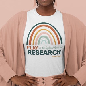May include: A white t-shirt featuring a colourful rainbow graphic and the text "PLAY is the highest form of RESEARCH - Albert Einstein".