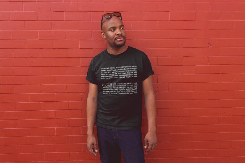 Puede incluir: Una persona lleva una camiseta negra con texto blanco que dice "Women's Rights Are Workers Rights Are Trans Rights Are Disability Rights Are Gay Rights Are Civil Rights Are Religious Rights Are Women's Rights Are Men's Rights Are Trans Rights Are".