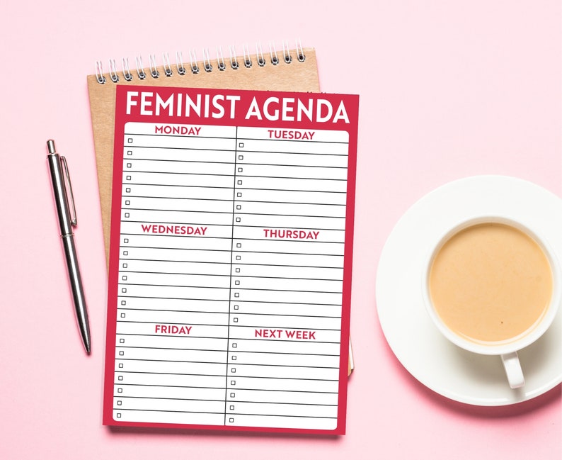 K&ouml;nnte beinhalten: Ein roter Planer mit dem Aufdruck "Feminist Agenda" auf der Vorderseite. Der Planer enth&auml;lt eine Liste der Wochentage mit leeren Zeilen zum Schreiben.