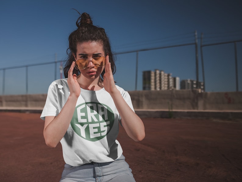 Puede incluir: Una camiseta blanca con un gr&aacute;fico circular verde que dice "ERA YES" en texto blanco.