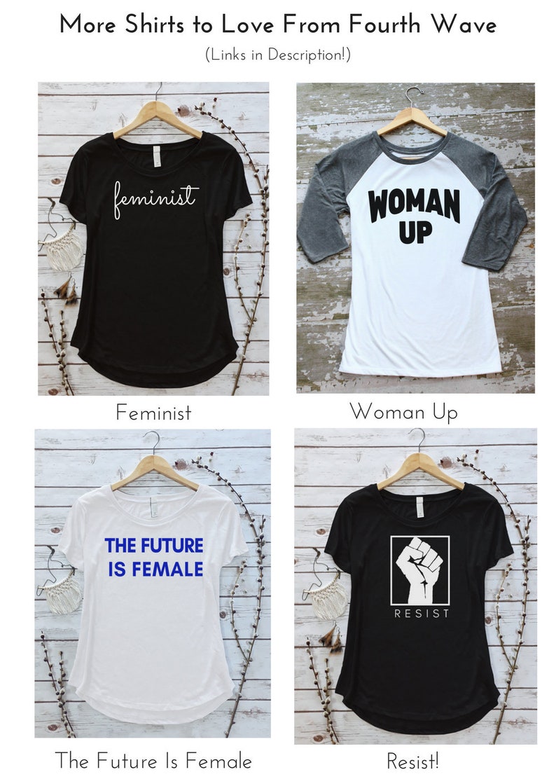 May include: Four different t-shirt designs with feminist themes. The shirts are displayed on hangers against a white wood background. The designs include "feminist", "woman up", "the future is female", and "resist" with a raised fist graphic.
