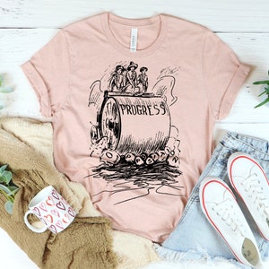 May include: A pink t-shirt with a black and white illustration of a steamroller labeled "Progress" crushing the word "Obstruction".