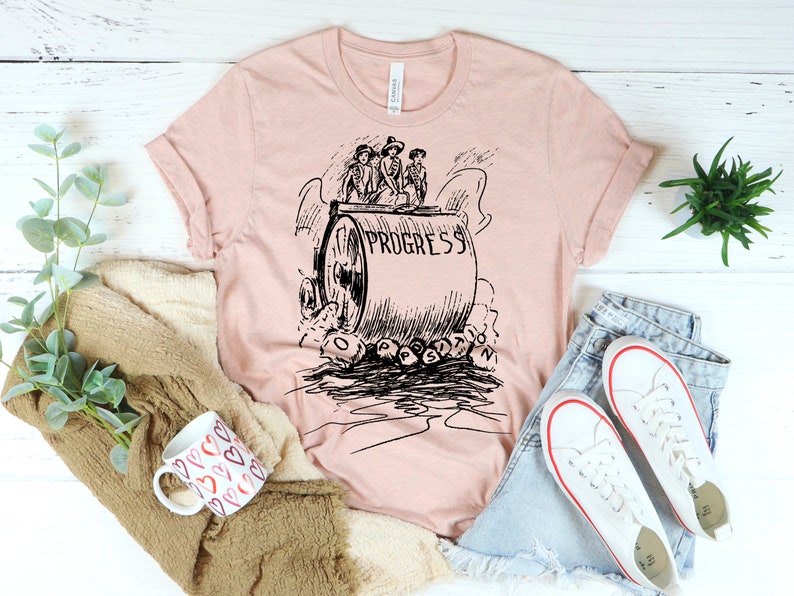 May include: A pink t-shirt with a black and white illustration of a steamroller labeled "Progress" crushing the word "Obstruction".