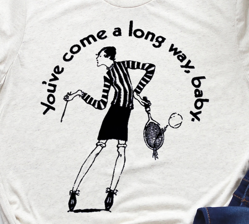 Puede incluir: Impresi&oacute;n gr&aacute;fica en blanco y negro de una mujer sosteniendo una raqueta de tenis con el texto "You've come a long way, baby."