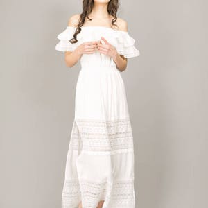 May include: A white off-the-shoulder maxi dress with lace trim and a side slit. The dress has a ruffled neckline and a flowing skirt.