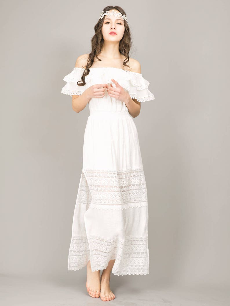 May include: A white off-the-shoulder maxi dress with lace trim and a side slit. The dress has a ruffled neckline and a flowing skirt.