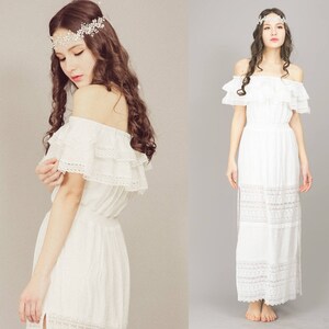 May include: Two women wearing white off-the-shoulder maxi dresses with lace trim. Both women are wearing headbands with rhinestones.