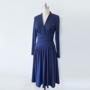 May include: A navy blue long-sleeved dress with a V-neckline and a wrap-style bodice. The dress has a fitted waist and a flowing skirt.